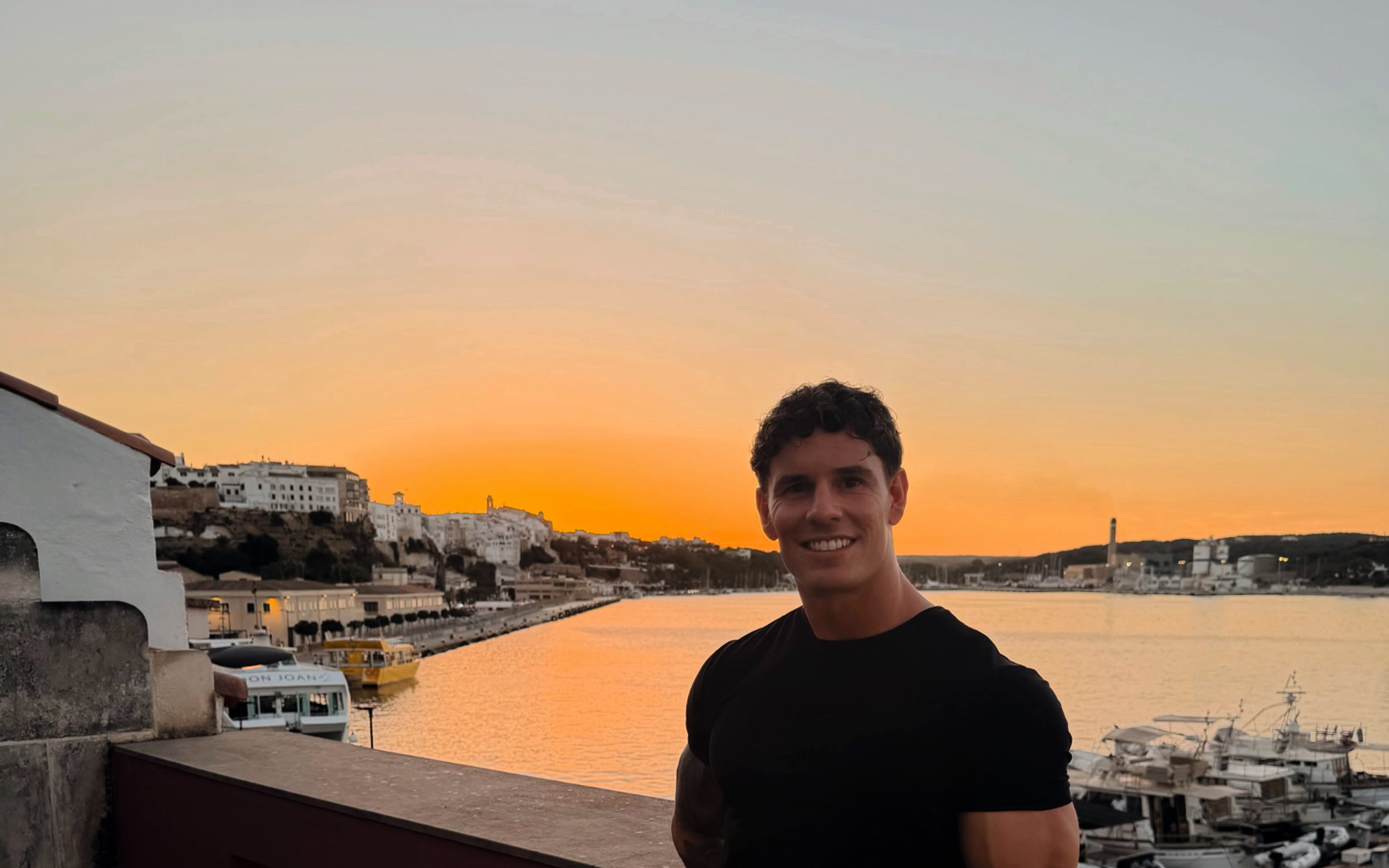 Luke Hayes smiling at golden hour, leaning on a harbour wall