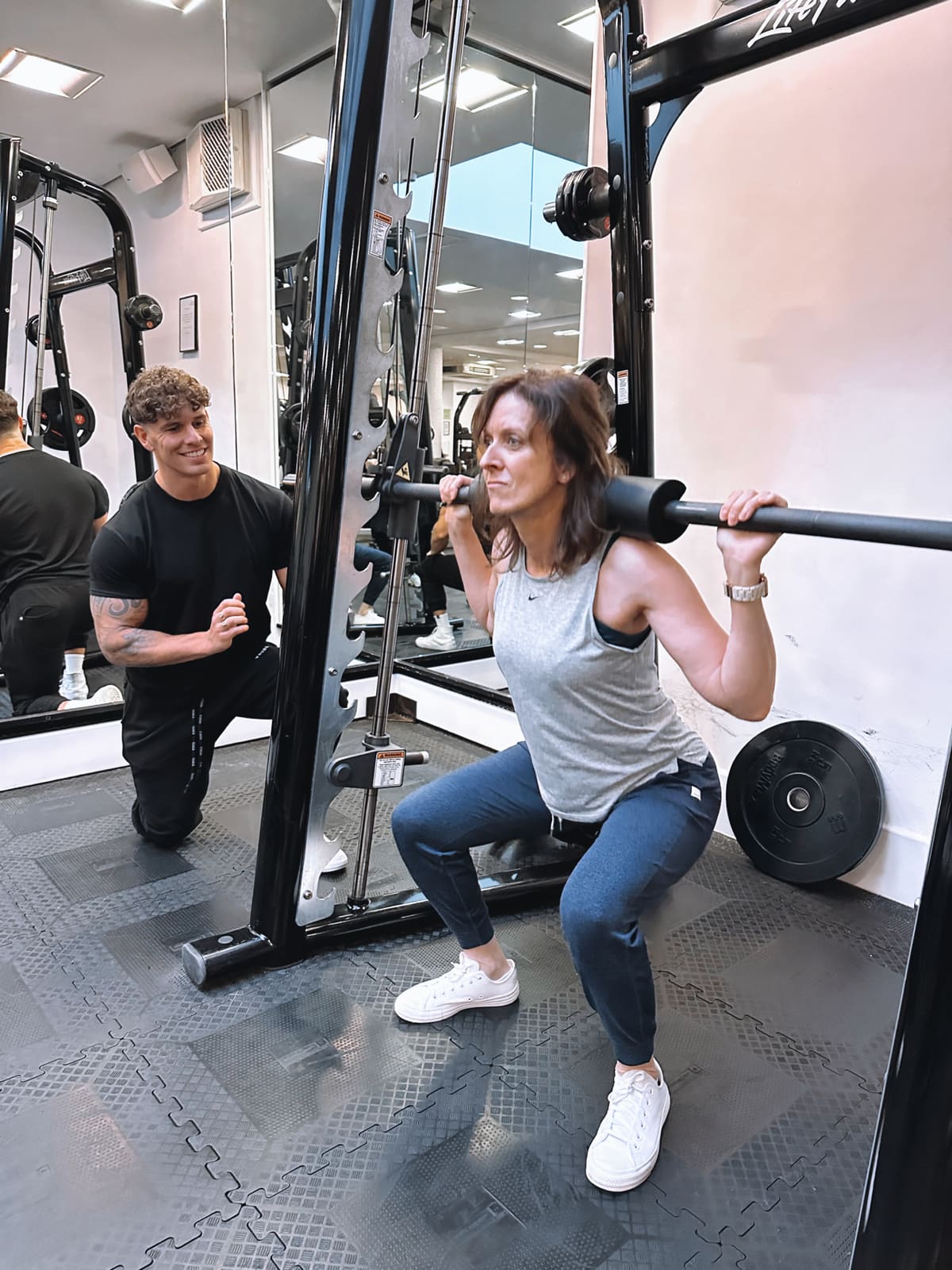 Luke kneeling beside a client, coaching her through a barbell squat